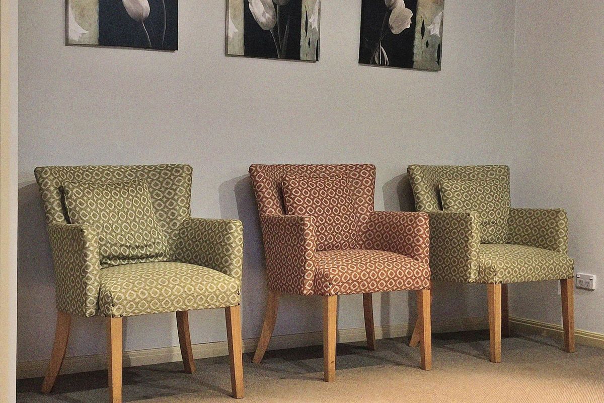 Three upholstered armchairs against a pale wall under framed flower prints, with no people.