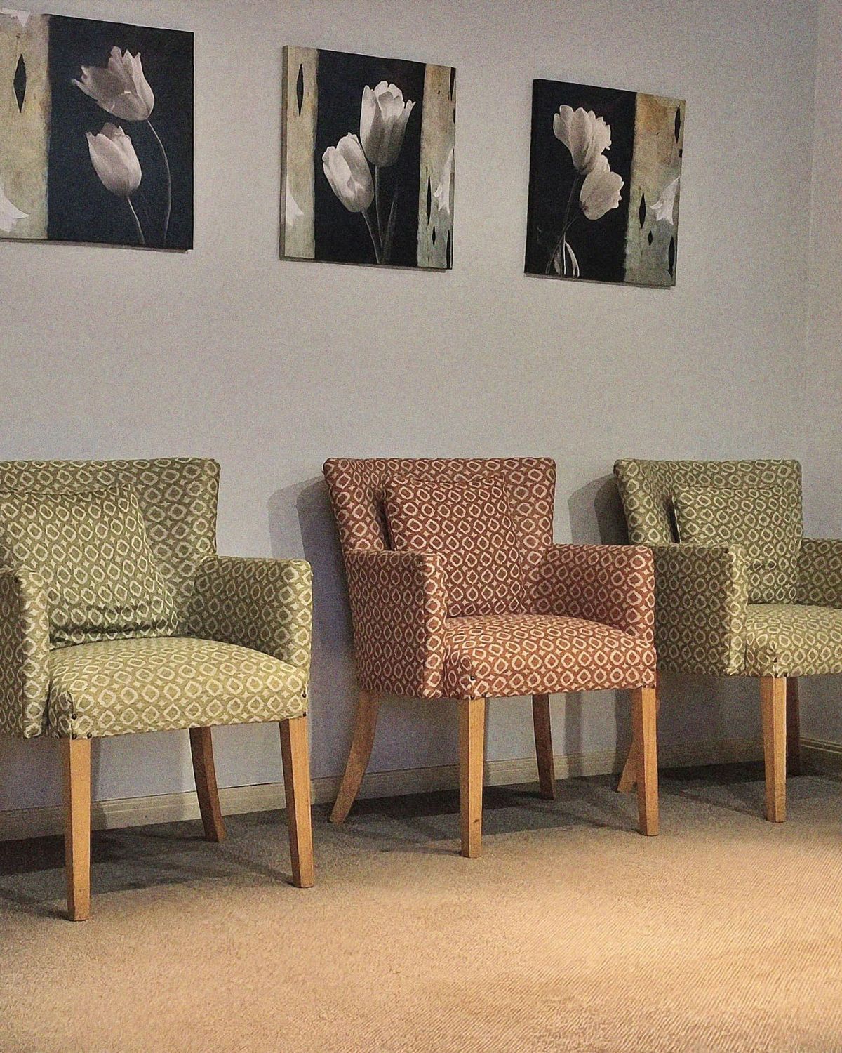 Three upholstered armchairs against a pale wall under framed flower prints, with no people.